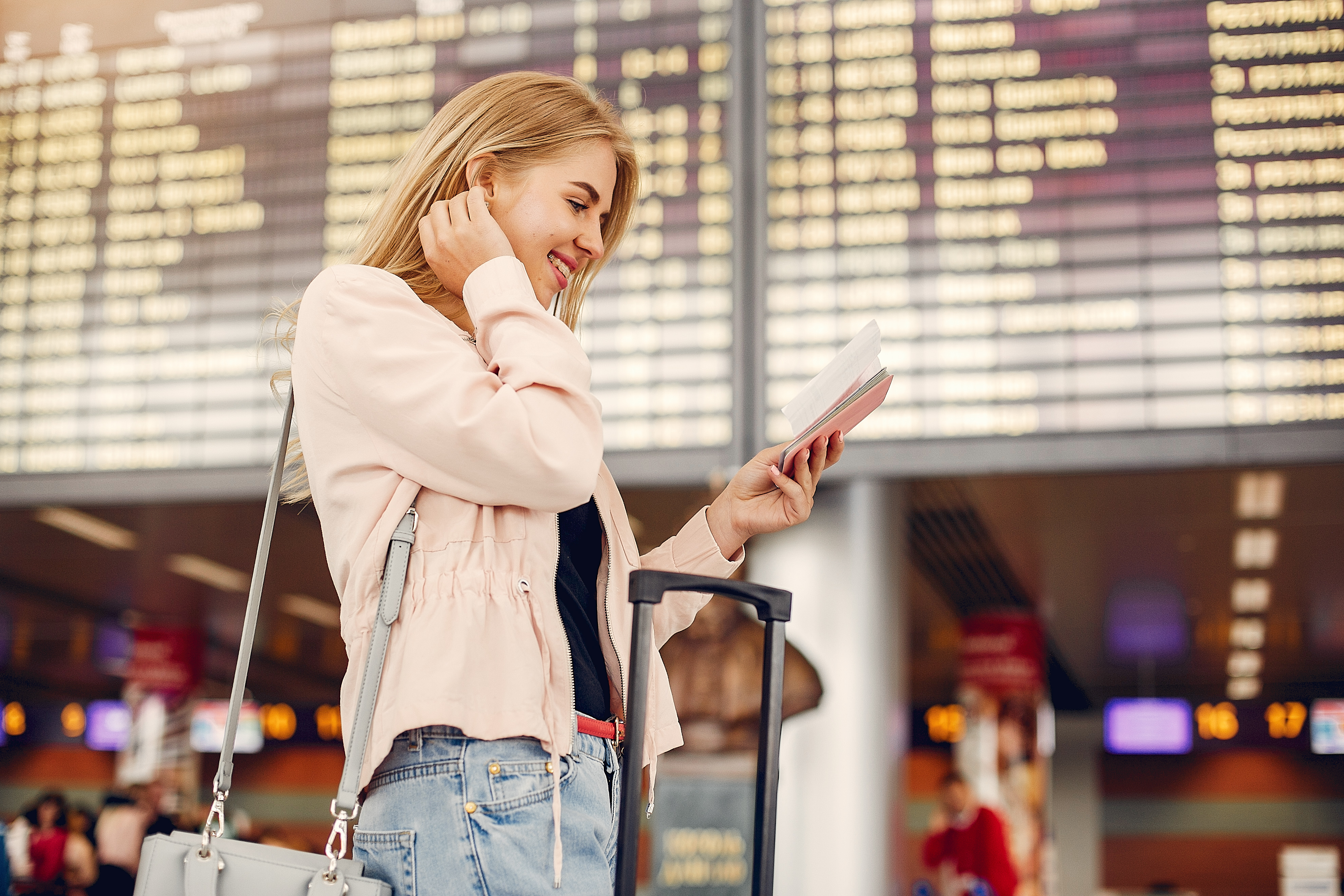 Solo female traveller standing beneath an airport departure board, checking flight details on her smartphone.